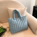 Light blue quilted puffer tote bag on a cozy white armchair with tulips for a lifestyle look - Light Blue