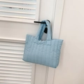 Detail van de lichtblauwe gewatteerde puffer-tas hangend aan een witte minimalistische deur - Blauw