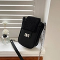 Black mini phone bag with studded flap and silver rotating lock on a white window sill - Black
