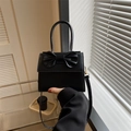 Detail einer schwarzen Mini-Handtasche aus PU-Leder mit Schleife, gehalten von Hand - Schwarz