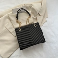 Bolso tote acolchado negro con cadena dorada sobre una chaqueta beige - Negro