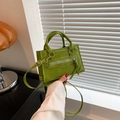 Mini bolso de mano verde hierba en cuero PU con asas y borla en un ambiente hogareño - Verde