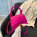 Détail d'un sac sablier rose vif avec poignée nouée posé sur un fauteuil gris - Rose Rouge