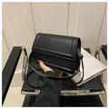 Close-up of minimalist black leather square bag with gold hardware on a modern chair - Black
