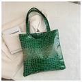 Primer plano de un bolso tote verde oscuro con textura de cocodrilo en un blazer - Verde