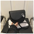 Minimalist black leather saddle bag with silver oval buckle on a stylish black chair - Black