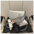 Metallic silver saddle bag with oval buckle and slim strap on a decorative book - Silver