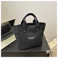 Primer plano del bolso tote de lona negra con letras blancas y remaches plateados - Negro