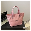Detalle de bolso tote de lona rosa con texto impreso en negro y remaches plateados en mesa - Rosa