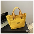 Close-up of yellow canvas tote bag with metal rivets and black slogan on wooden table - Yellow