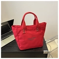 Detalle del bolso tote de lona roja con remaches plateados y texto negro en un escritorio - Rojo