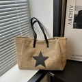 Grande borsa tote in paglia intrecciata con stella nera e doppi manici in ambiente luminoso - Nero