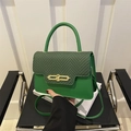 Detail of green hard-shell box bag showing woven black texture and golden metal lock - Green