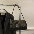 Detail of black crocodile texture shoulder bag featuring gold hardware on clothing rack - Black