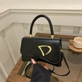 Detail of black leather crossbody bag with iconic gold D-buckle on a wooden table - Black