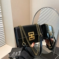 Elegant black glossy shoulder bag with gold chain strap and geometric lock shown in mirror - Black