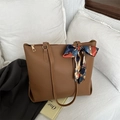 Borsa tote in ecopelle marrone con foulard decorativo appoggiata a un cuscino bianco - Cuoio