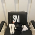Zwarte leren schoudertas met witte SM-letters en kettingriem in een moderne lifestyle-setting - Zwart