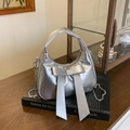 Sac demi-lune argenté avec gros nœud et chaîne sur fond de livre d'art moderne - Argenté