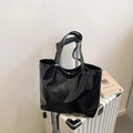 Glossy black large tote bag with adjustable straps on a suitcase in a minimalist setting - Black