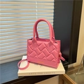 Pink crossbody bag with woven texture and top handle on a white book backdrop - Pink