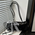 Schicke glänzende schwarze Schultertasche mit weißer Spitzenschleife auf einer Fensterbank - Schwarz