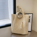 Große beige geflochtene Strohtasche mit Quastenanhänger auf einem Metalltisch - Mit Anhänger / Cremeweiß