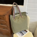 Olive green tote bag with striped handles and silver logo on a white chair - Green