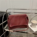 Dunkelrote Umhängetasche aus geflochtenem Leder mit Goldkette auf modernem Regal - Rote gewebte Kettentasche mit Klappe / Rot