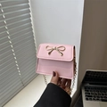 Mini borsa a tracolla rosa con fiocco dorato e catenella sottile, tenuta in mano - Rosa