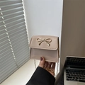 Mini beige saddle bag with golden bow buckle and chain strap shown in a lifestyle setting - Khaki