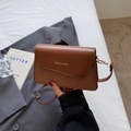 Brown leather crossbody bag with woven texture and gold lettering in a lifestyle setting - Brown