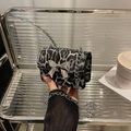 Mini leopard print crossbody bag with silver bow clasp and chain strap held in hand - Black