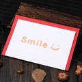 White cutout 'Smile' greeting card with a bright red envelope on a wooden desk - Smile Design (308#smile)