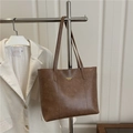 Borsa tote in ecopelle marrone con logo dorato esposta su un supporto di metallo - Cachi