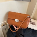 Elegant brown leather crossbody bag with silver buckle held in a minimalist setting - Brown