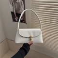 Close-up of white minimalist baguette bag featuring golden metal lock and leather texture - White