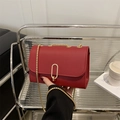 Elegant red leather crossbody bag with gold chain strap and stylish oval metal clasp - Red
