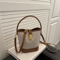 Sac seau en cuir marron et toile beige avec ferrures dorées sur un livre - Marron