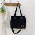 Bolso tote de pana negra con correa ajustable y etiqueta de marca sobre un gancho - Negro
