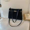 Sac cabas minimaliste en daim noir avec boucles dorées présenté sur un canapé en tissu - Noir
