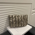Clutch trapuntata color oro champagne con finitura metallica posata su un libro bianco - Oro
