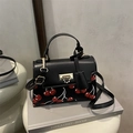 Borsa a tracolla retrò nera con stampa ciliegia e fibbia dorata su una pila di libri - Nero