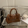 Borsa a tracolla marrone scuro lucida con fibbia argento e cinturino su uno scaffale - Marrone