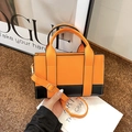Detail view of a contrasting orange and black handbag with gold hardware and shoulder strap - Orange (Orange/Black Block)
