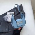 Detail view of light blue crescent underarm bag with gold buckle on a grey blazer background - Blue