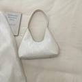 Close-up of a white textured underarm bag with brand lettering on a fabric background - White