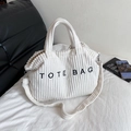 White corduroy tote bag with black embroidery and adjustable strap in a cozy home setting - White