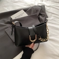 Chic black matte underarm bag with a bold gold U-shaped buckle on a grey blazer - Black