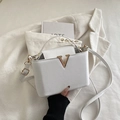 Sac seau chic blanc grainé avec détail V doré posé sur une veste en velours - Blanc Cassé